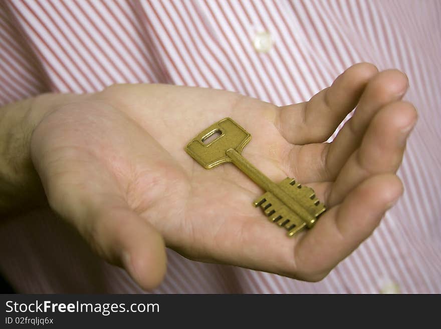 Gold old house key in the palm of a young man in a striped shirt on a green background. Gold old house key in the palm of a young man in a striped shirt on a green background