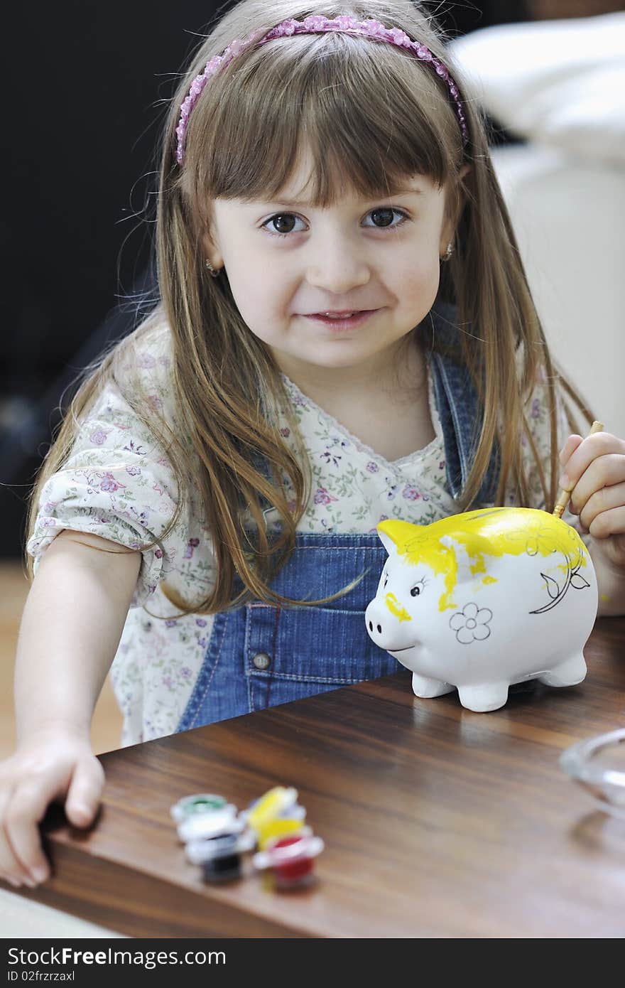 Happy young girl  portrait at home while painting piggy bank and representing banking and finance concept. Happy young girl  portrait at home while painting piggy bank and representing banking and finance concept