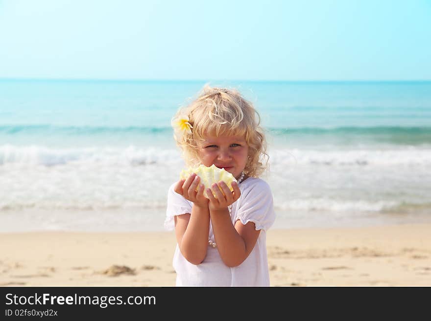 Little girl with white curly hair on the beach with a seashell. Little girl with white curly hair on the beach with a seashell