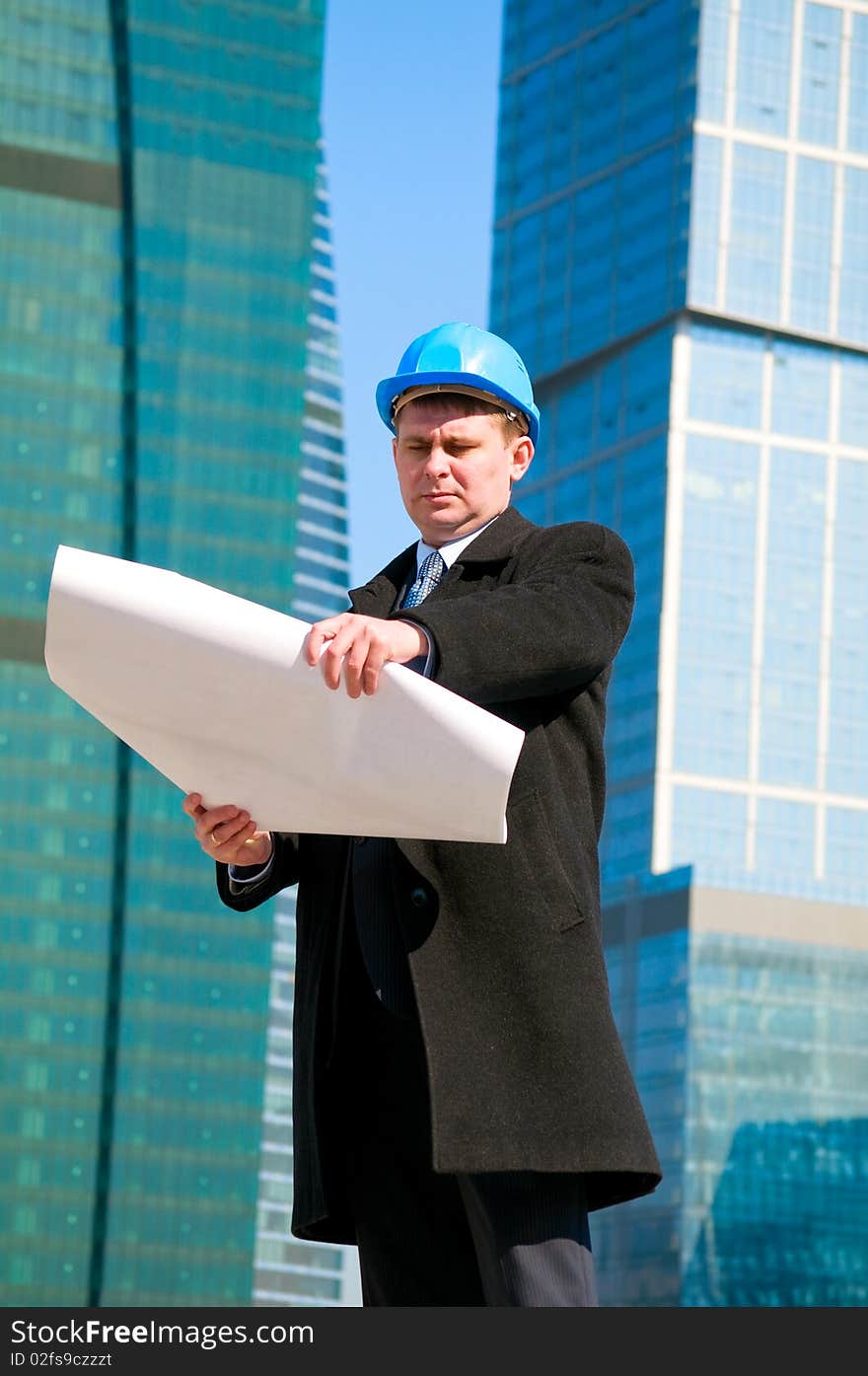 Engineer with blue hard hat holding drawing on skyscrapers background