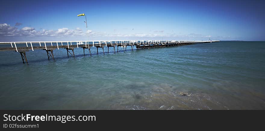 Very long pier stretching into the blue sea from the shore with white railings. Very long pier stretching into the blue sea from the shore with white railings