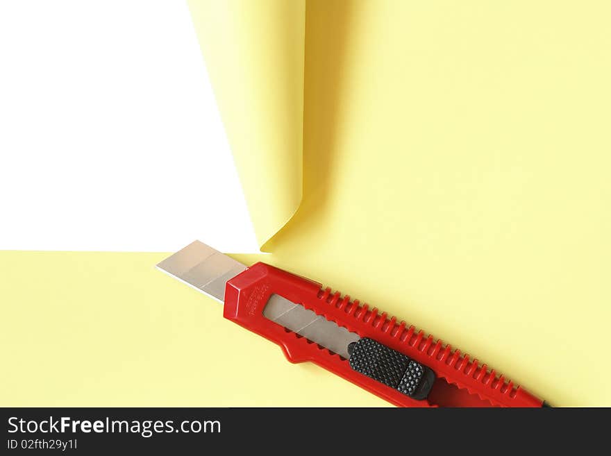 Red office knife cutting yellow paper sheet. Isolated on white with clipping path. Red office knife cutting yellow paper sheet. Isolated on white with clipping path