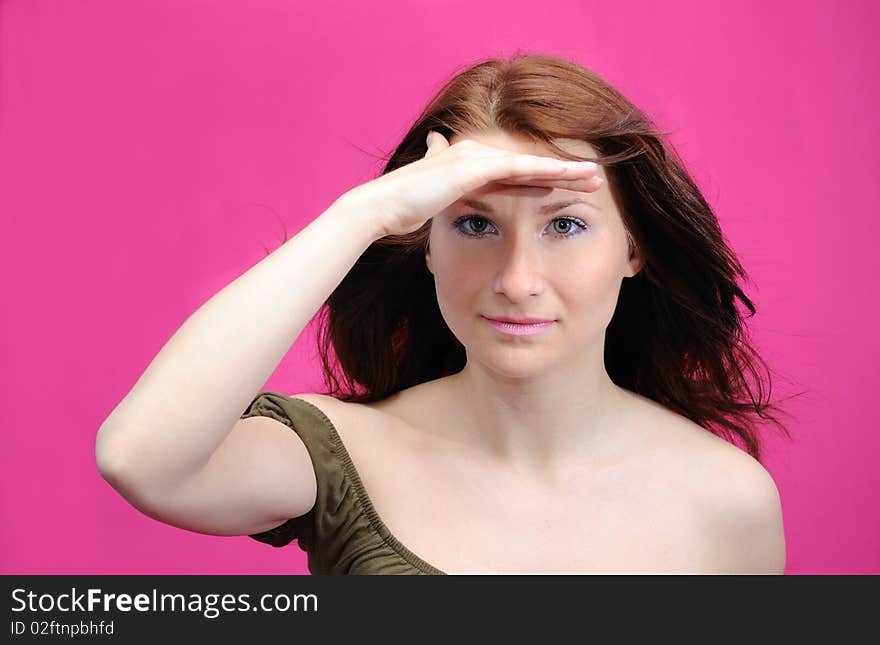 The girl has put a palm to the face and looks afar. A pink background. The girl has put a palm to the face and looks afar. A pink background