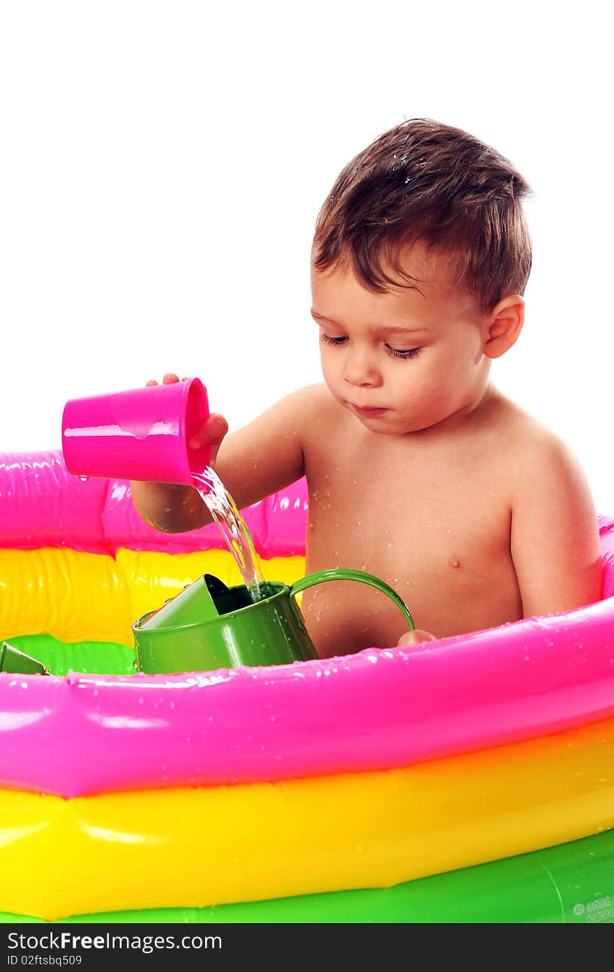 A toddler pouring water from one container into another while sitting in a brighly colored kiddie pool. Isolated on white.