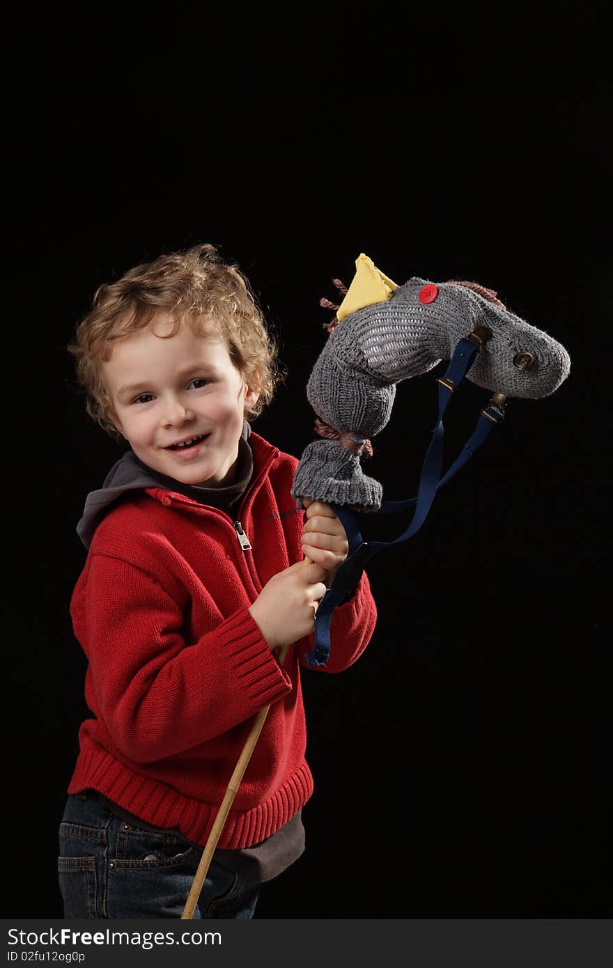 Young white boy playing with horse made of a sock on black background. Young white boy playing with horse made of a sock on black background