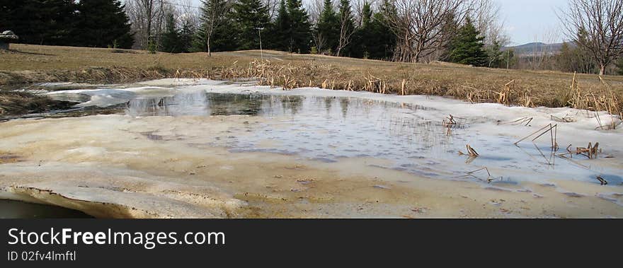 A pond is melting in spring, in rural Quebec. A pond is melting in spring, in rural Quebec