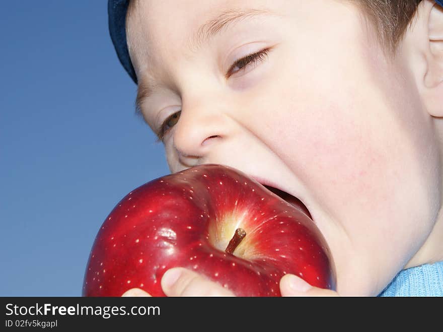 The child eagerly bites big red apple, the background sky. The child eagerly bites big red apple, the background sky