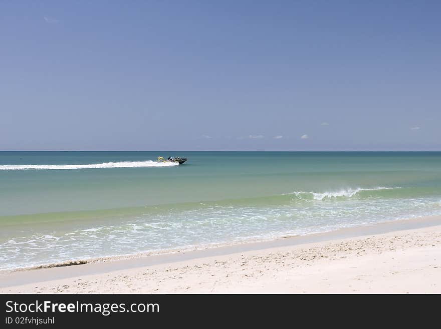 A speed motor boat cruising in the sea. White sand beach, turquoise ocean and blue sky.