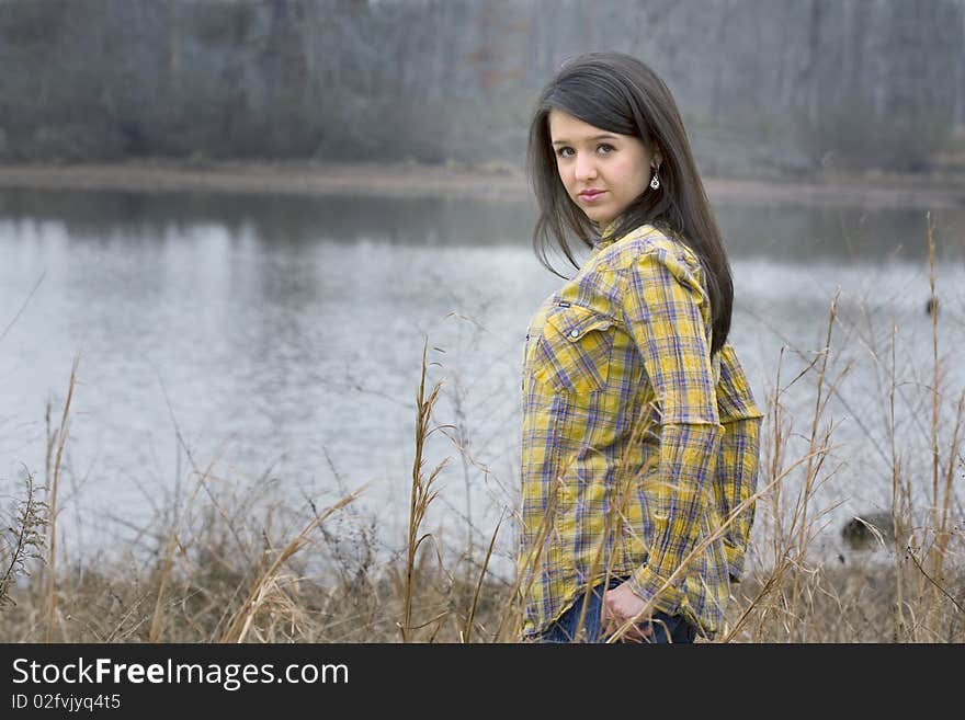 Beautiful young brunette woman with hands in pockets standing in front of lake. Beautiful young brunette woman with hands in pockets standing in front of lake