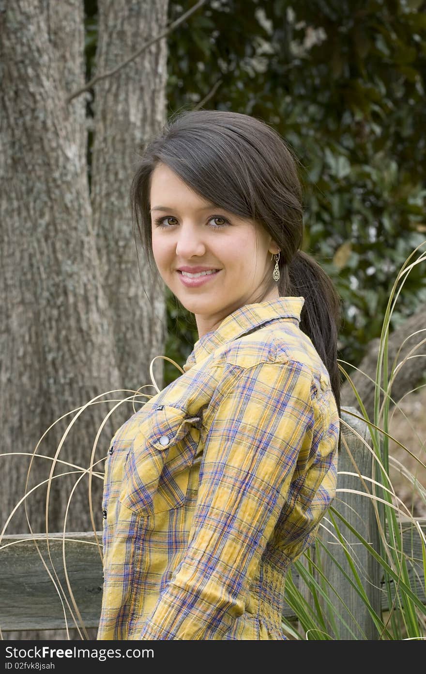 Young woman with brown hair and eyes in yellow shirt standing by old rustic fence. Young woman with brown hair and eyes in yellow shirt standing by old rustic fence