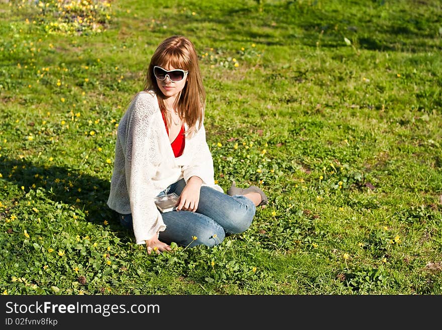 A girl in white woman's jacket sits on a green grass. A book on knees. A girl in white woman's jacket sits on a green grass. A book on knees.