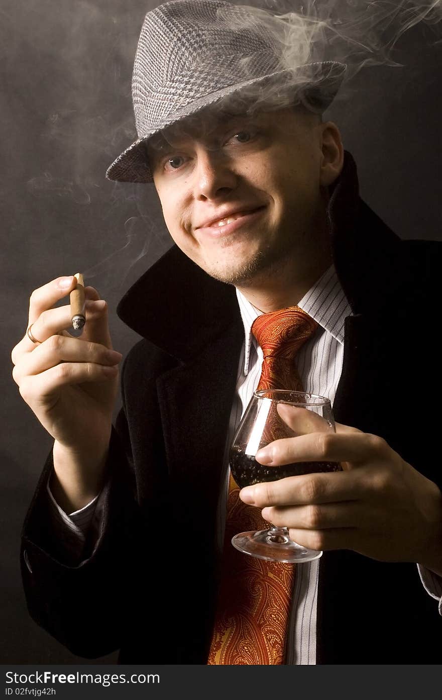 Elegant, handsome, young businessman. Wearing hat, necktie and black coat, holding cigar and drink. Elegant, handsome, young businessman. Wearing hat, necktie and black coat, holding cigar and drink.