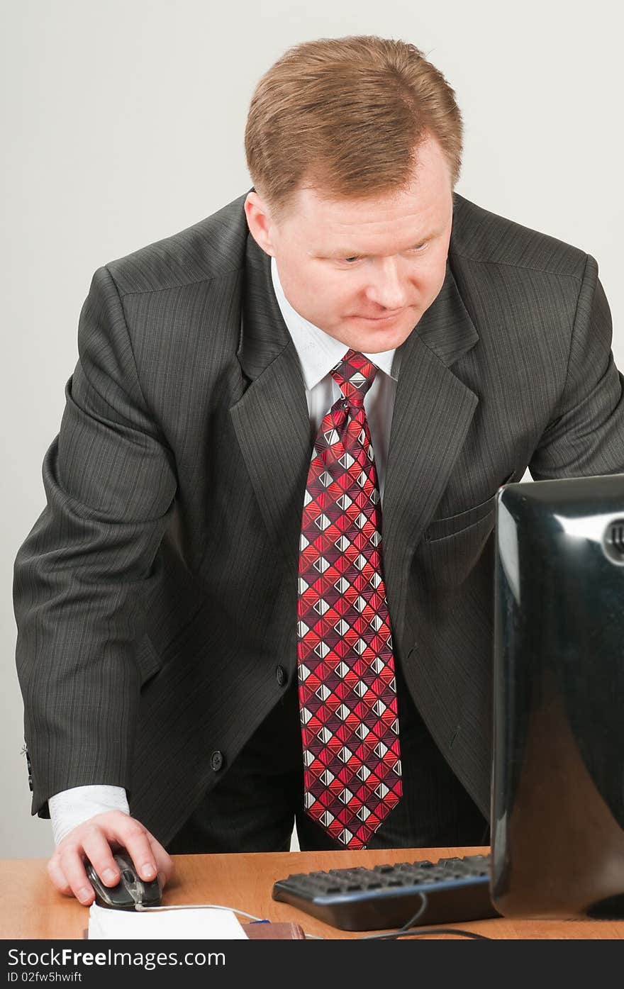 The man of forty five years in a grey suit and a red tie works on the computer. The man of forty five years in a grey suit and a red tie works on the computer.