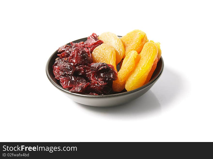 Red ripe dried cranberries and dried apricots in a small black bowl on a reflective white background. Red ripe dried cranberries and dried apricots in a small black bowl on a reflective white background