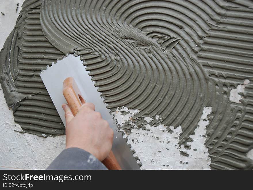 Man's hand spreading thinset mortar on cement board using notched trowel. Man's hand spreading thinset mortar on cement board using notched trowel.