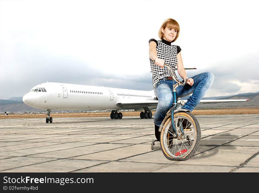 Young woman on bike on a runway smiling on a background of the plane