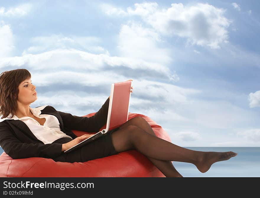 Attractive businesswoman lying on a red sofa holding a notebook. Image taken on a dreamy background with sky and sea. Attractive businesswoman lying on a red sofa holding a notebook. Image taken on a dreamy background with sky and sea.