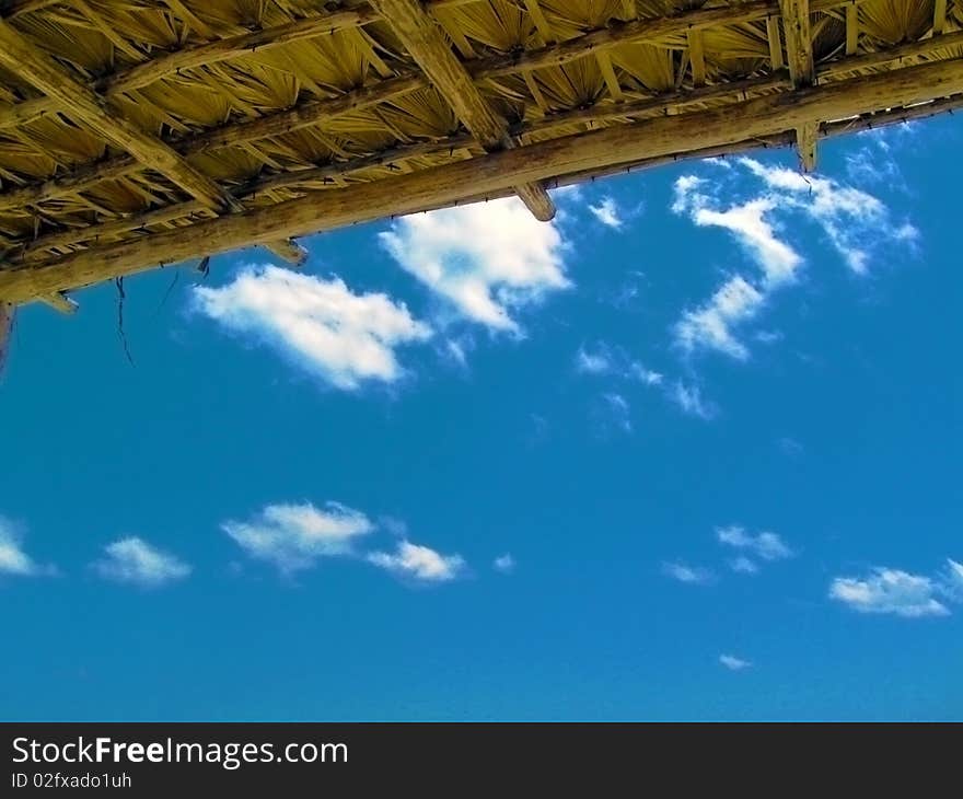 Blue sky with just a few puffy white clouds under a hut roof. Blue sky with just a few puffy white clouds under a hut roof