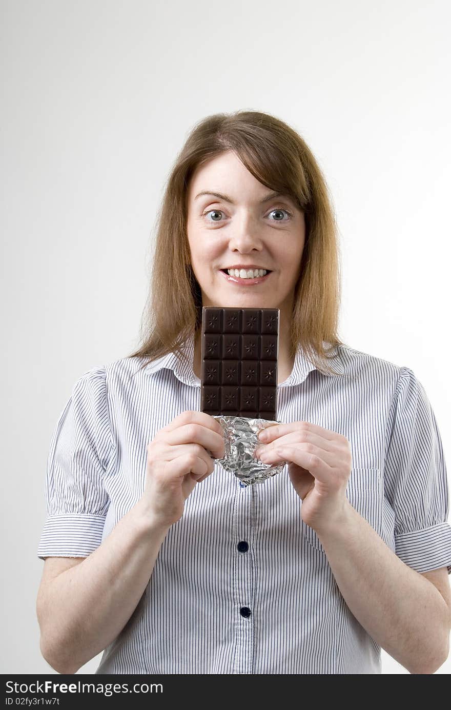 A vertical image of a pretty young woman smiling with a large bar of chocolate in her hand preparing to enjoy her treat. A vertical image of a pretty young woman smiling with a large bar of chocolate in her hand preparing to enjoy her treat