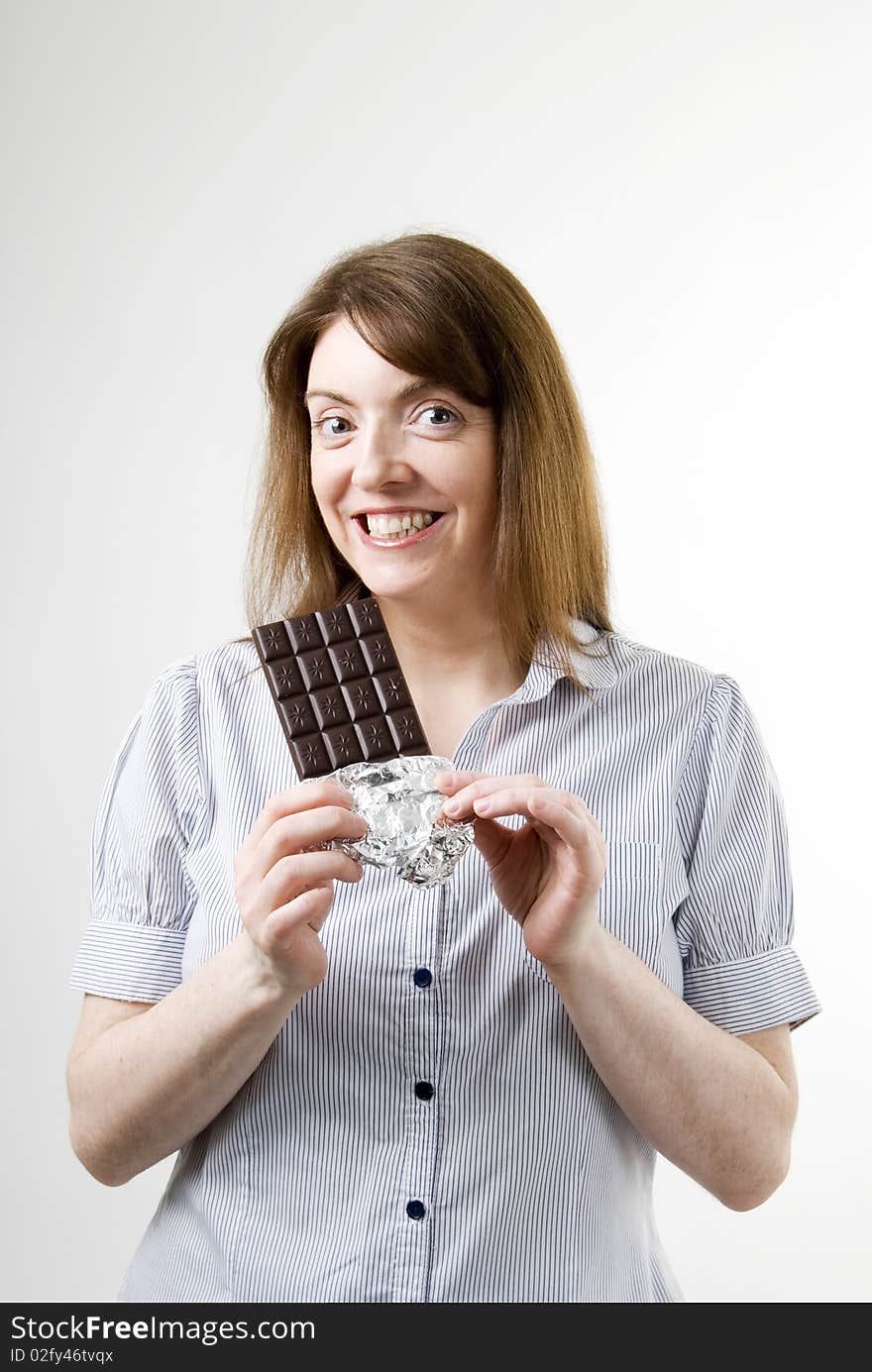 A vertical image of a pretty young woman happy and smiling in anticipation of the delicious chocolate bar she is holding and about to eat