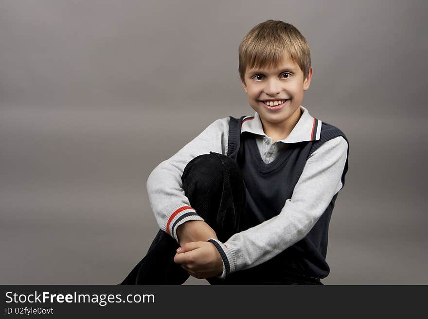 Cute and happy teenager boy with positive facial expression sitting and laughing isolated over gray background. Cute and happy teenager boy with positive facial expression sitting and laughing isolated over gray background