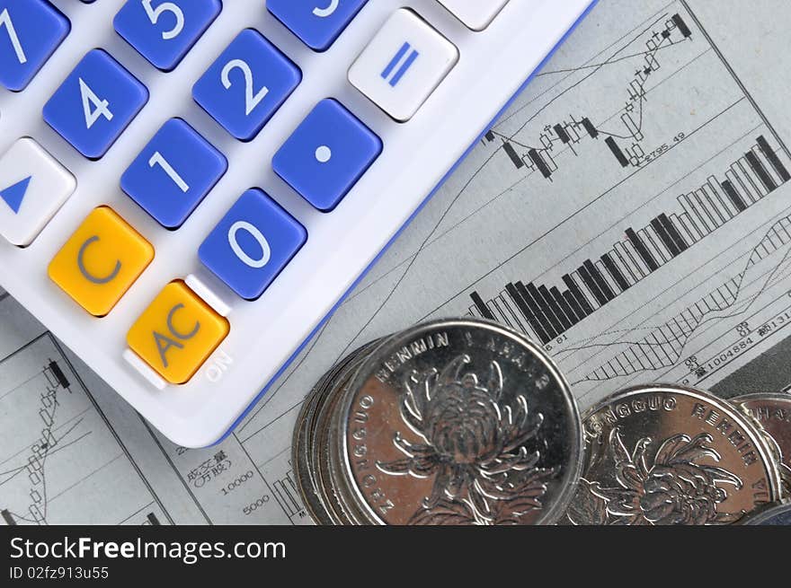 A calculator and some coins put on a sheet with stock chart, means business, finance, money, stock market statistic, and calculating. A calculator and some coins put on a sheet with stock chart, means business, finance, money, stock market statistic, and calculating.