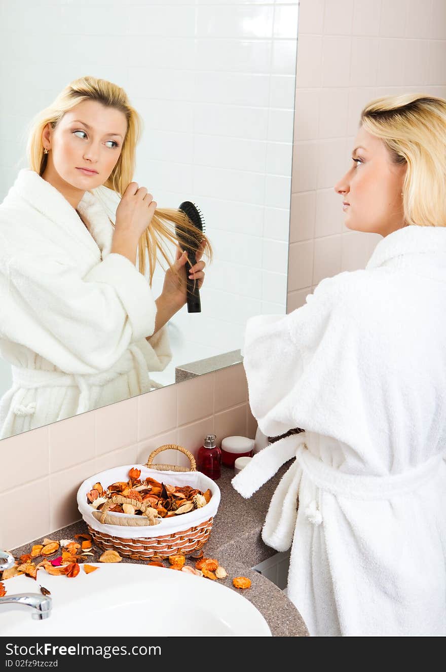 A young woman brushing hair in front of a bathroom mirror. Vertical shot.