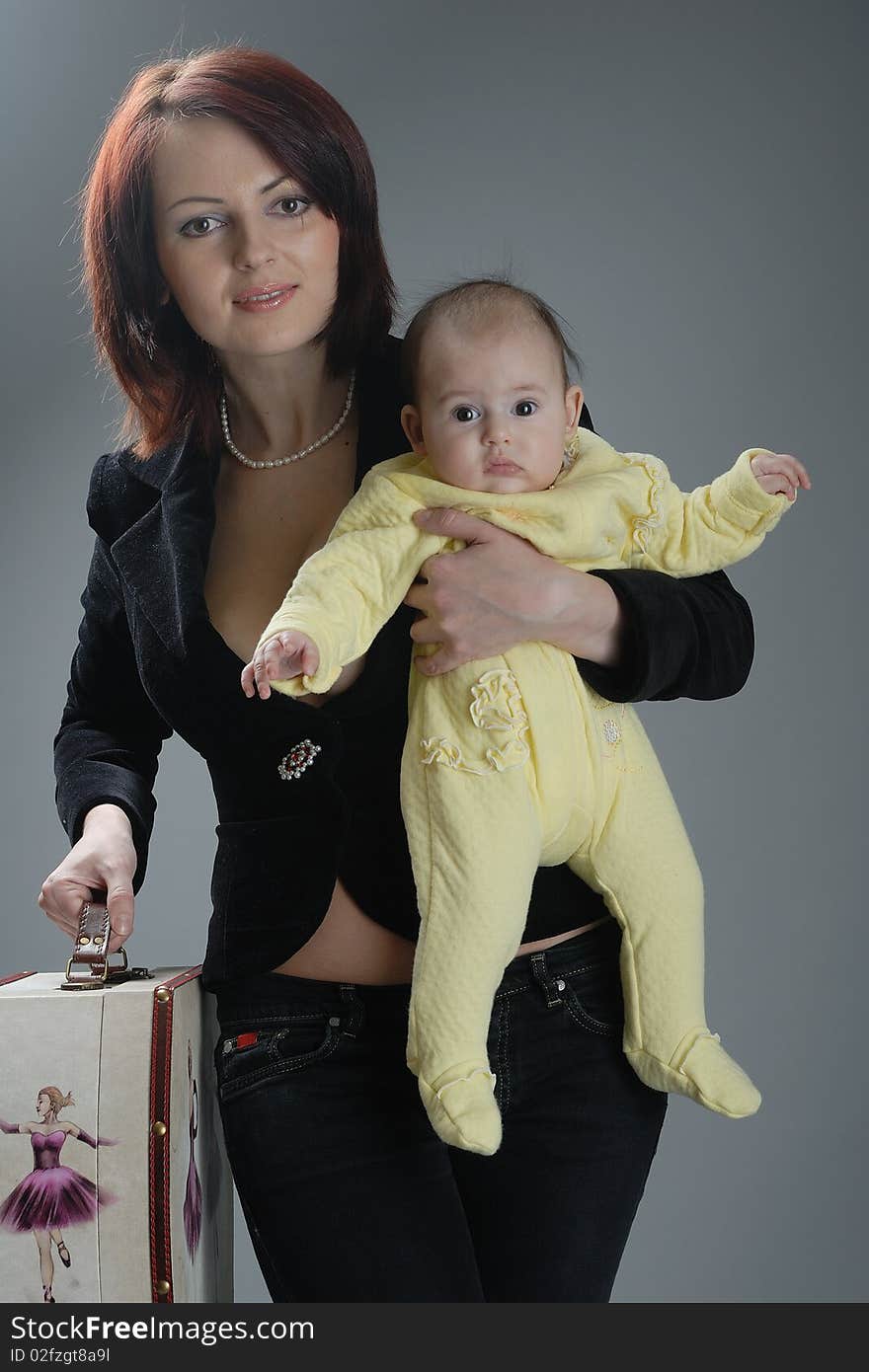 Woman with child and suitcase on grey background