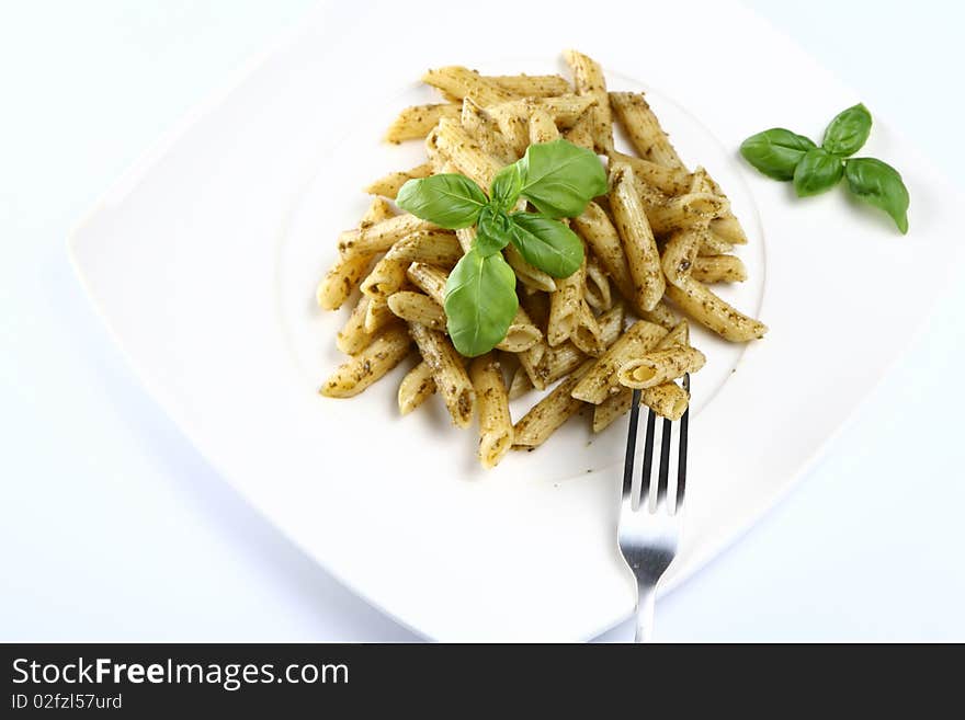 Penne with pesto decorated with basil on a plate with a fork