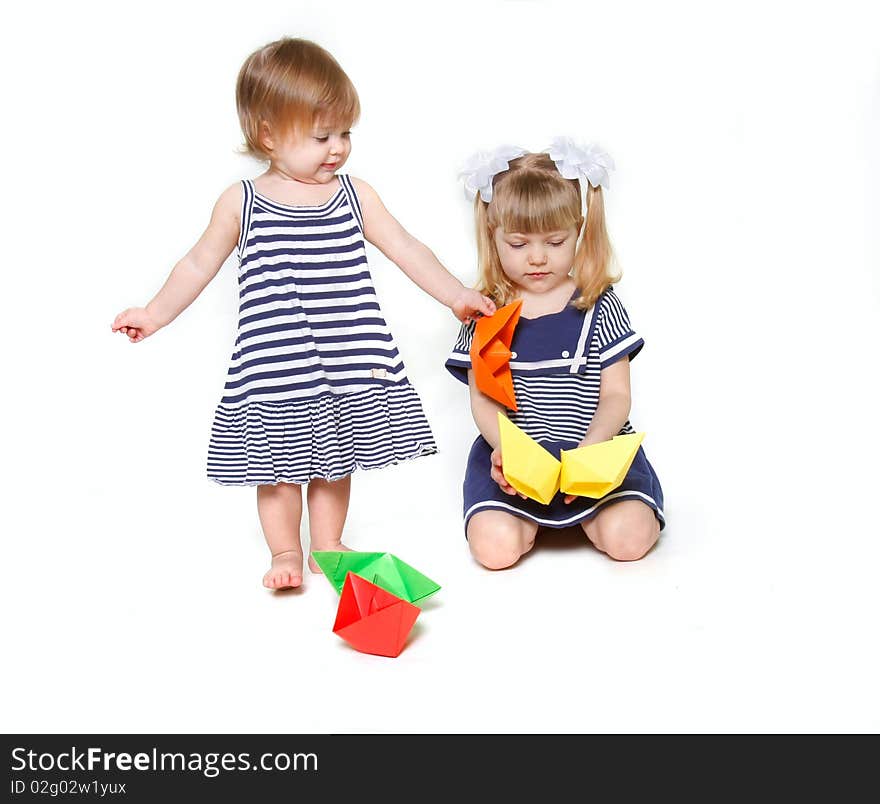 Two sisters in sailor dresses with paper ships over white