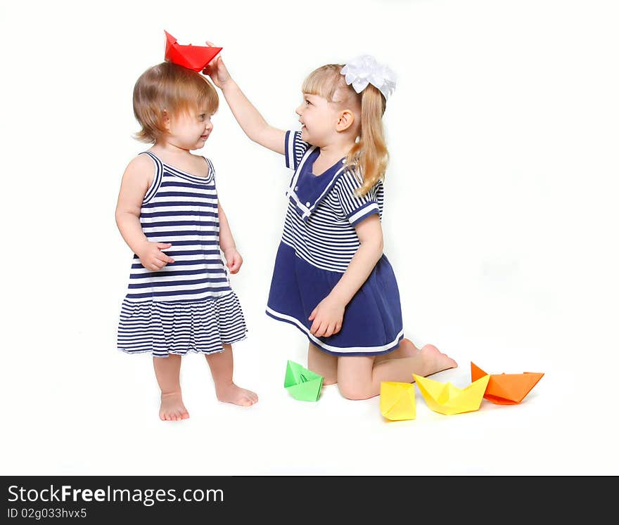 Two young sisters in sailor dresses with paper ships over white. Two young sisters in sailor dresses with paper ships over white