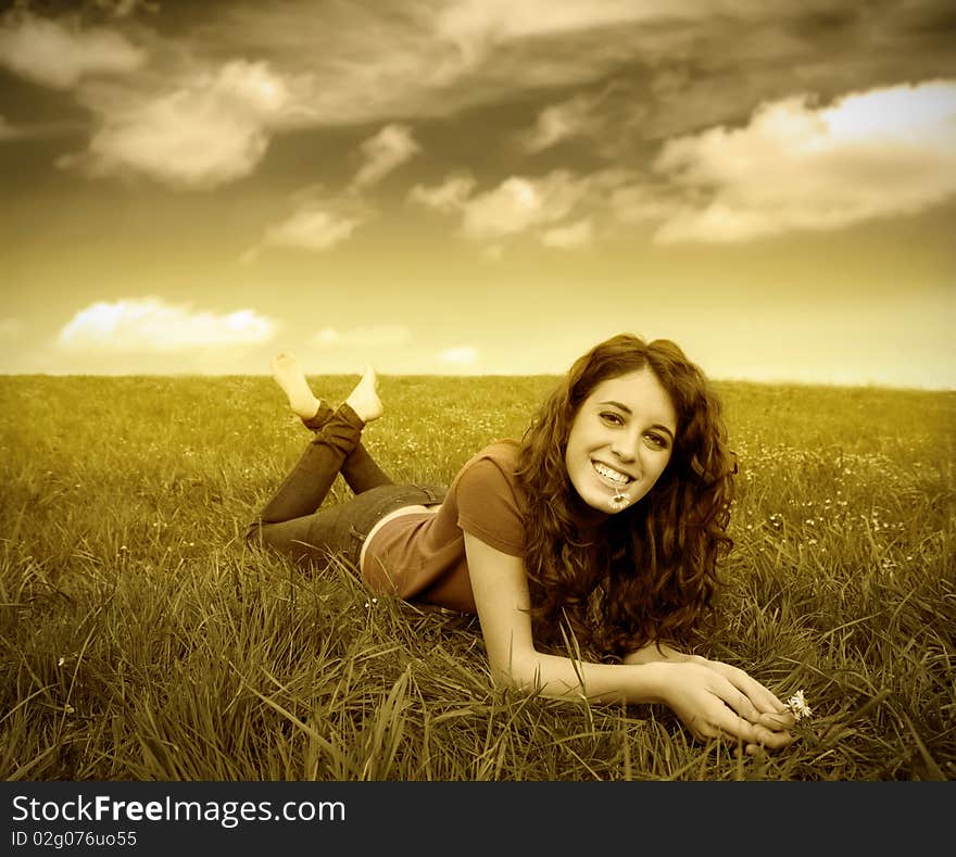 Smiling young woman lying on a meadow with a daisy in her mouth. Smiling young woman lying on a meadow with a daisy in her mouth