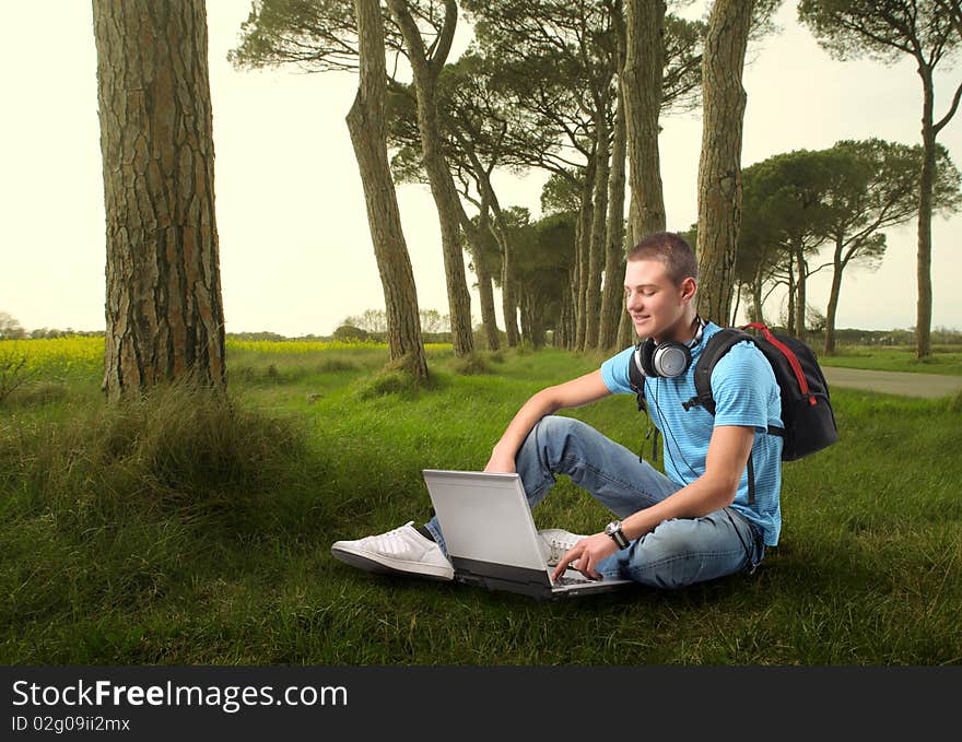 Young man sitting on a green meadow and using a laptop. Young man sitting on a green meadow and using a laptop