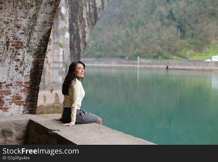 Smiling woman sitting under an ancient bridge