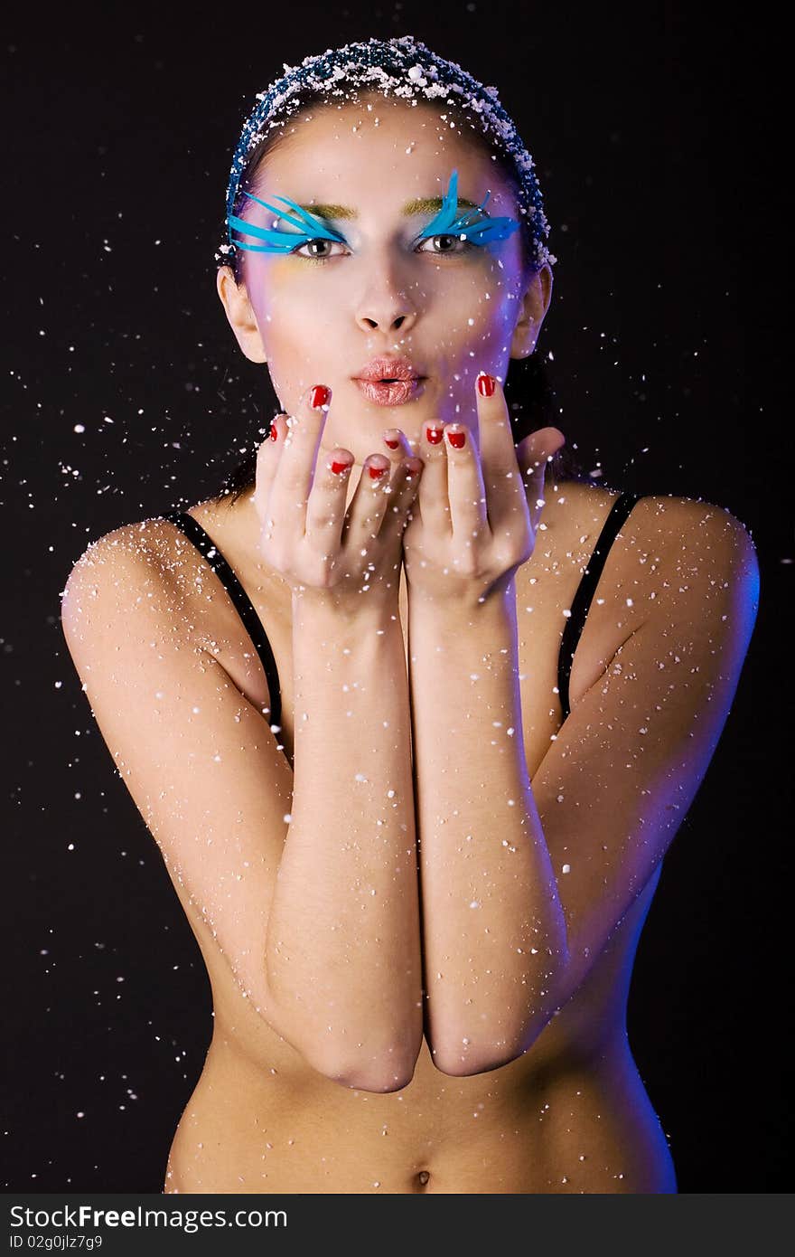 The girl with creative make-up blows white snowflakes with palms. Dark background. The girl with creative make-up blows white snowflakes with palms. Dark background.