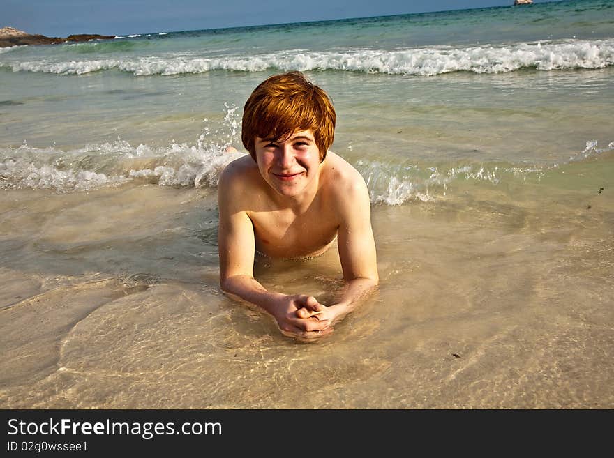 Boy in bathingsuit is lying at the beach and enjoying the saltwater with tiny waves and smiles. Boy in bathingsuit is lying at the beach and enjoying the saltwater with tiny waves and smiles