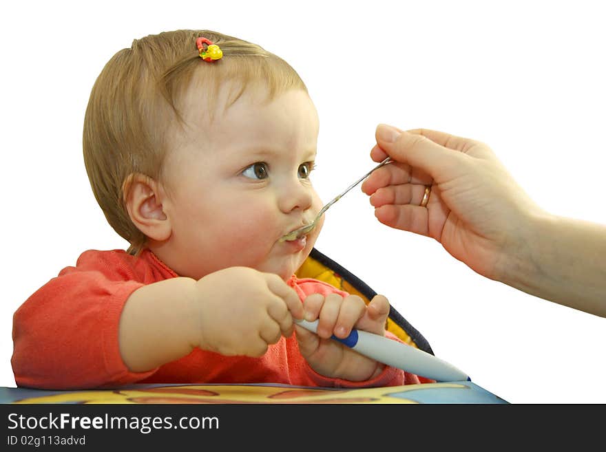 The child with a hairpin in hair sits at a table and he is fed with mum. The child with a hairpin in hair sits at a table and he is fed with mum