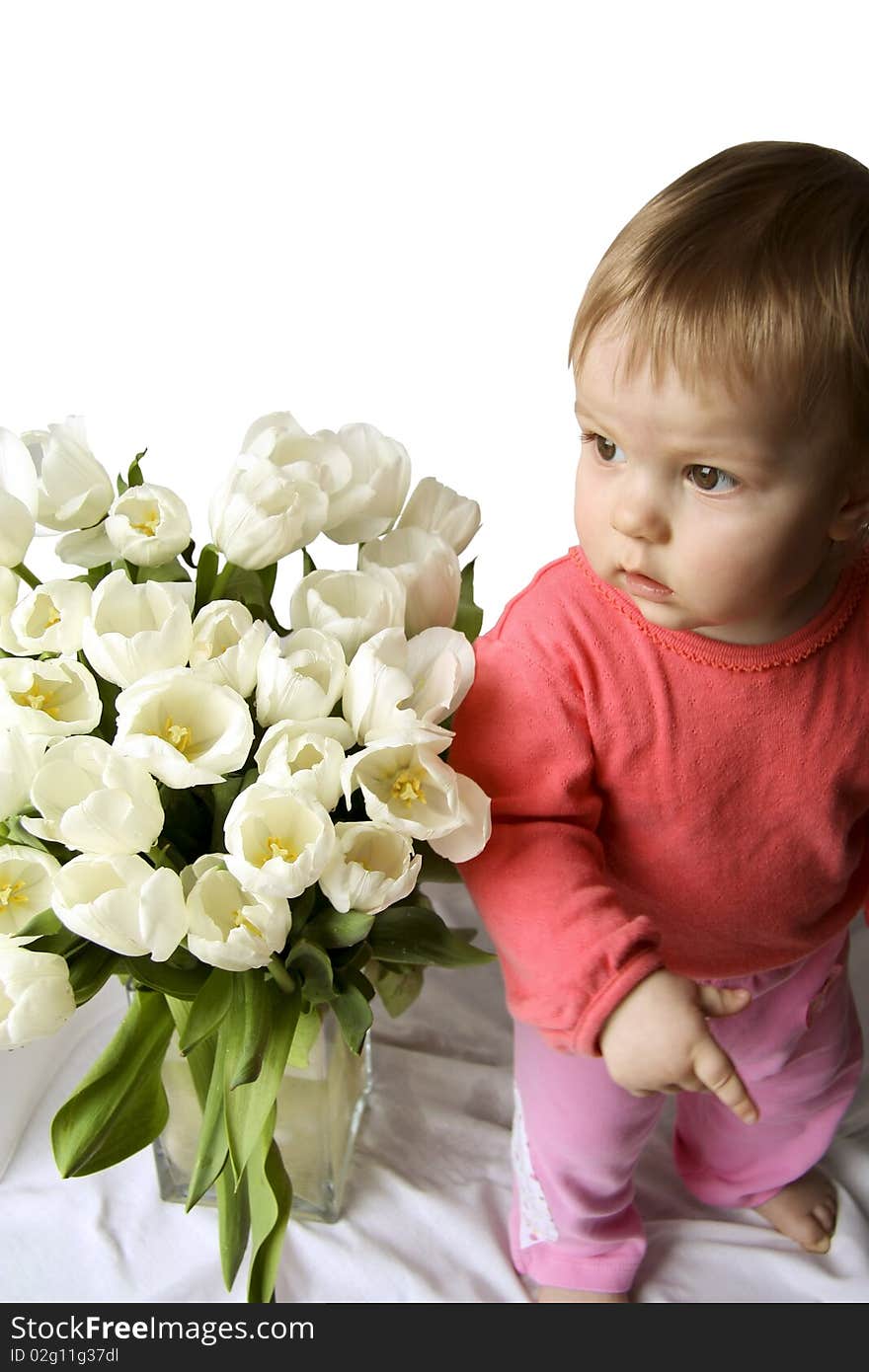 The child with white tulips looks aside and shows an index finger. The child with white tulips looks aside and shows an index finger