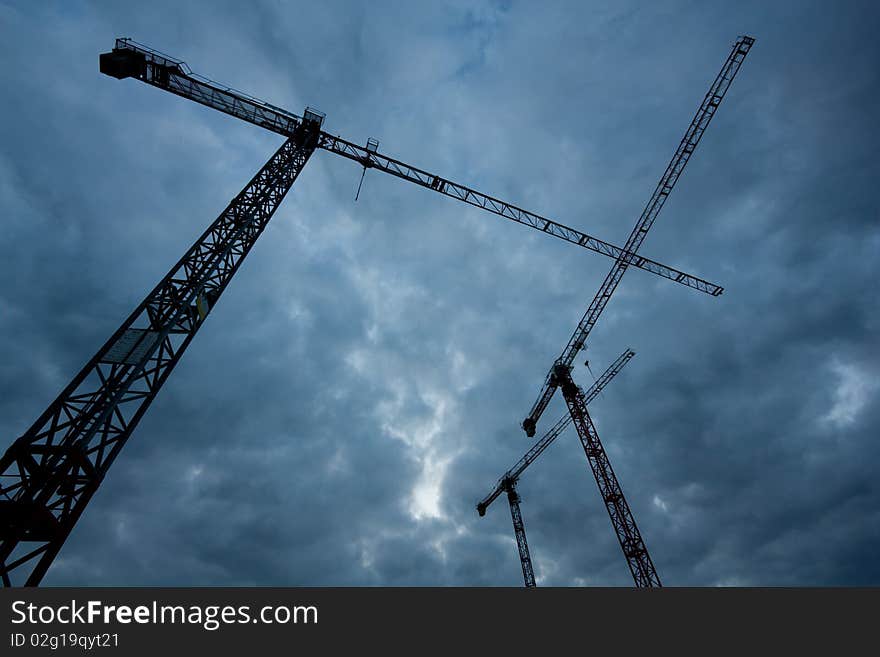 Three cranes under a stormy sky, shot from the ground up.