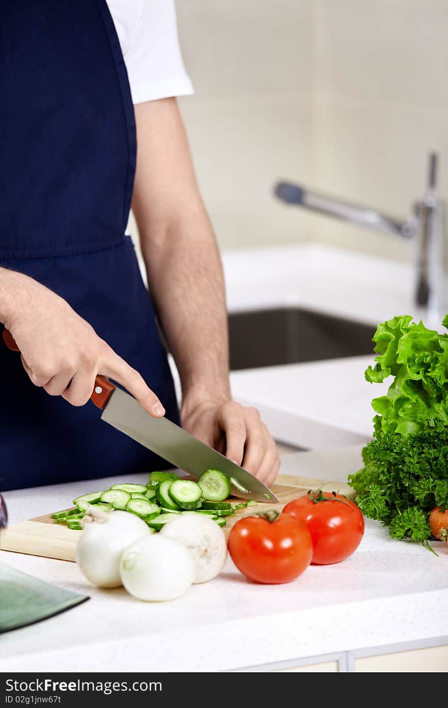 The man in an apron cuts cucumbers close up. The man in an apron cuts cucumbers close up