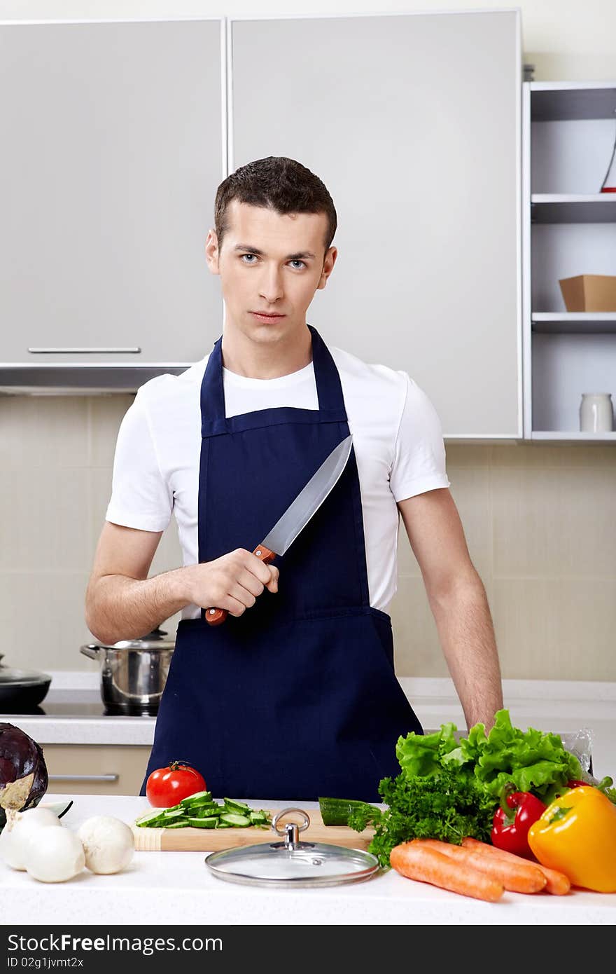 The young man in an apron with a knife at kitchen. The young man in an apron with a knife at kitchen