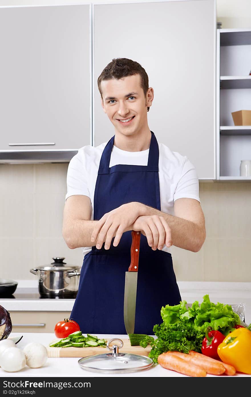 The young man in an apron with a knife at kitchen. The young man in an apron with a knife at kitchen