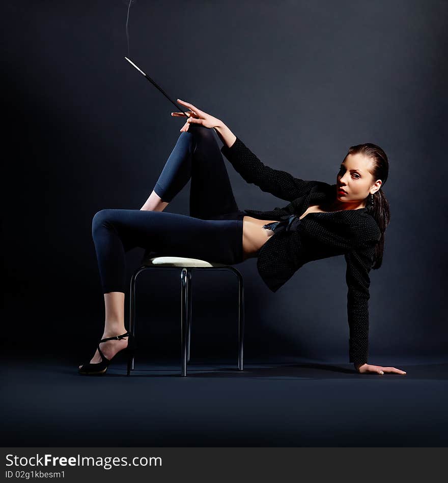 The portrait of a slim young lady in dark clothes holding a lighted cigarette in her hands. The portrait of a slim young lady in dark clothes holding a lighted cigarette in her hands