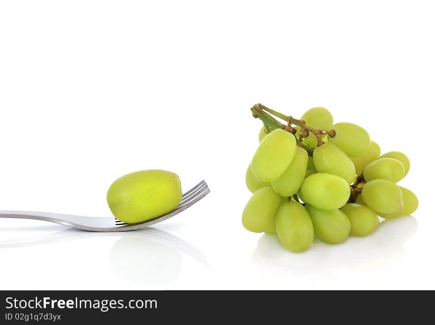 Bunch of green grapes with one on the end of a stainless steel fork, isolated over white background with reflection. Bunch of green grapes with one on the end of a stainless steel fork, isolated over white background with reflection.