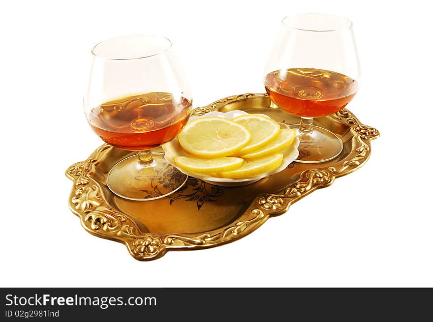 Two glasses of cognac with lemon on a tray on a white background. Two glasses of cognac with lemon on a tray on a white background