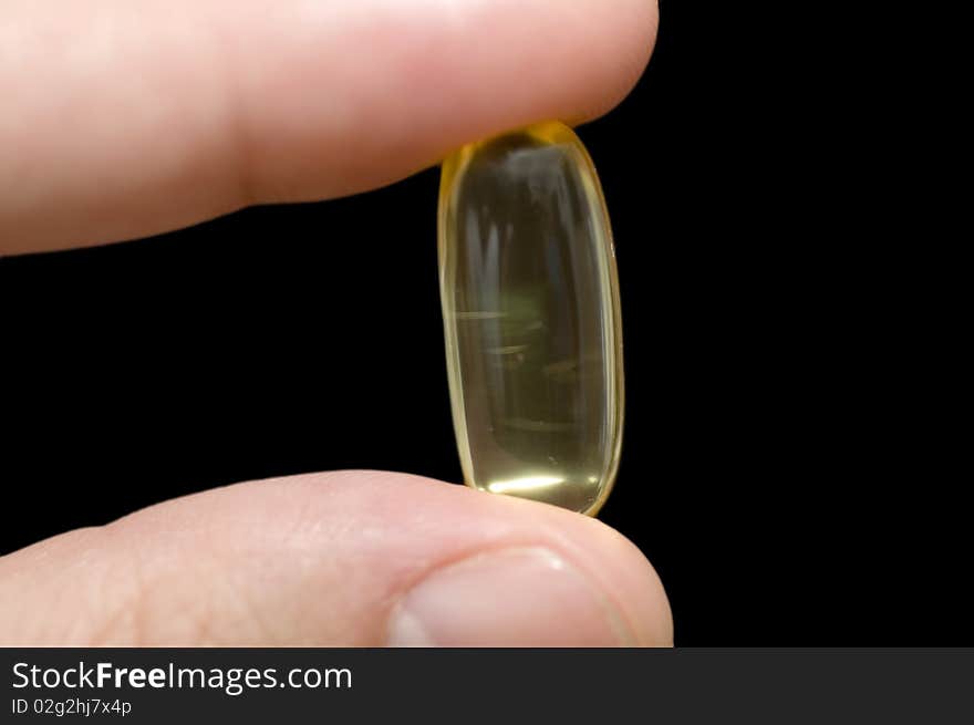 Hand holding a pill on black background