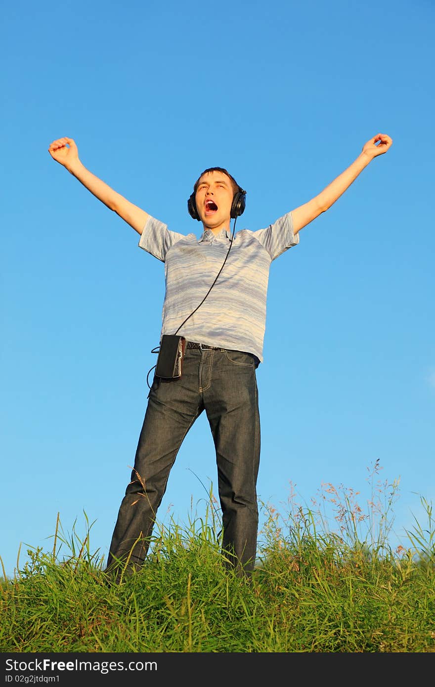 One handsome man is standing on a meadow with raised hands. headphones on his hand.