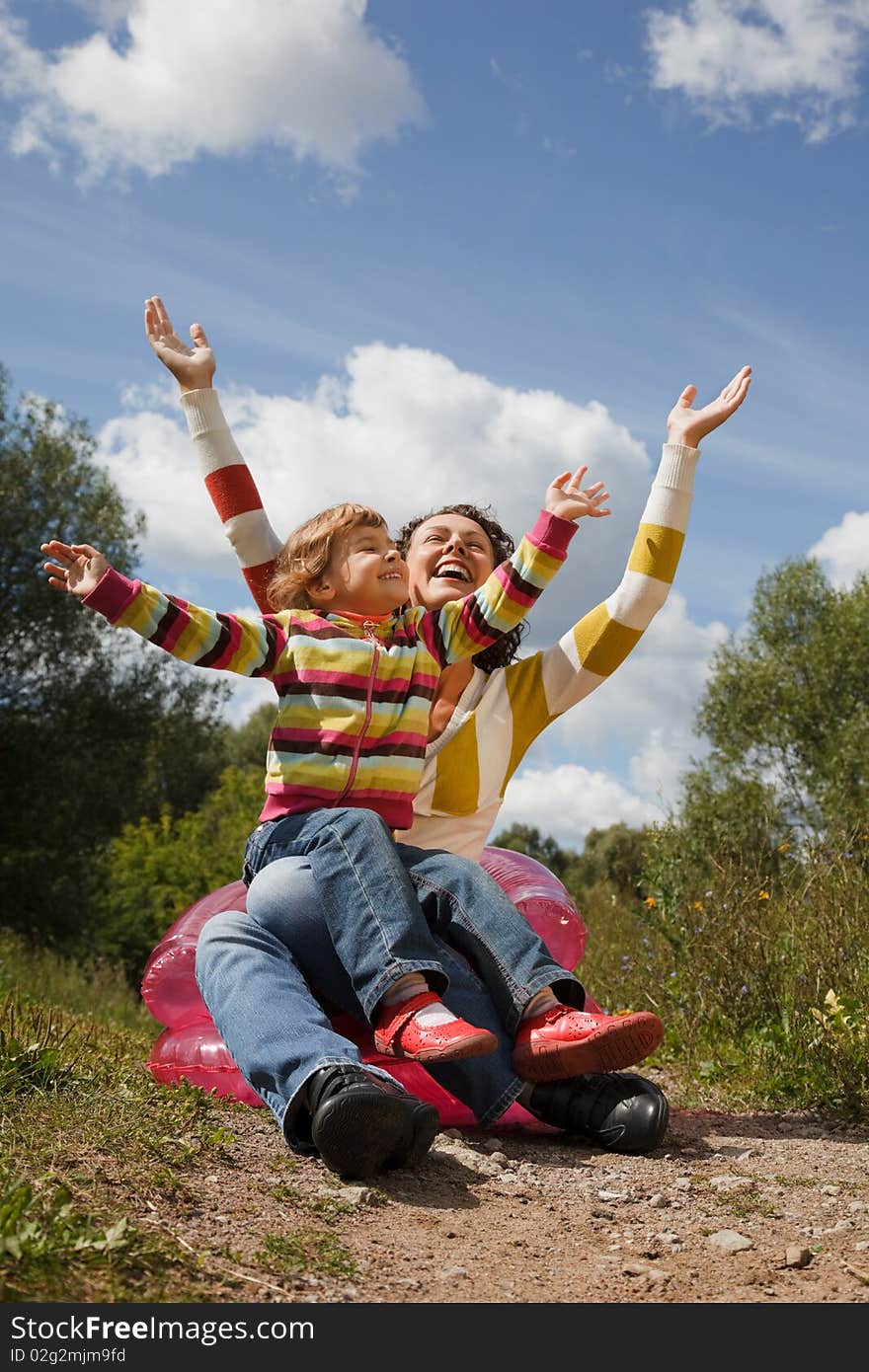 Mother and daughter play in the open air, sitting on an inflatable armchair. hands up