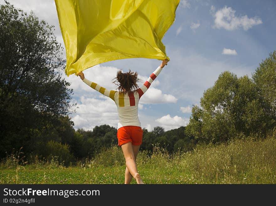 Young woman in sunny summer day runnig with yellow fabric in hand, whiffle fabric. Young woman in sunny summer day runnig with yellow fabric in hand, whiffle fabric