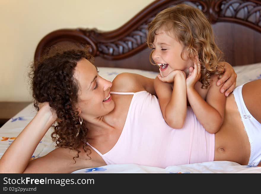 Laughing young mother and daugther lying and embracing on bed in hotel room.